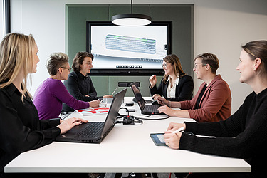 Das Bild zeigt das BIM Team in einer Besprechung. Im Hintergrund ist ein BIM-Modell zu erkennen.
