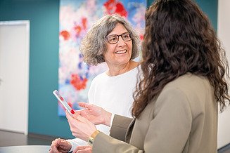 Eine erfahrene Ingenieurin steht an einem Stehtisch und bespricht mit anderen Professionals die Planung digitaler Baumodelle.