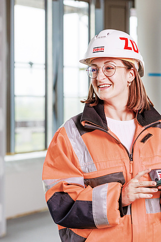 Larina, Auszubildende Bauzeichnerin bei der Zentralen Technik, steht mit einem Tablet auf der Baustelle.