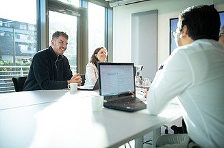 Gut gelaunte Mitarbeitende aus dem Bauingenieurswesen sitzen in einem Besprechungsraum, der von der Morgensonne erleuchtet wird.
