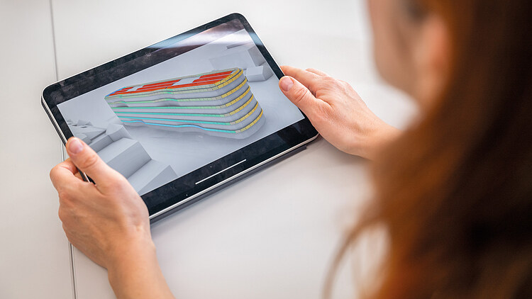 Auf dem Bild ist eine Frau zusehen, die ein Tablett hält. Auf dem Tablett ist ein digitales Modell des Gebäudes Z2 zu sehen.