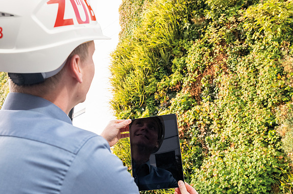 The picture shows a person standing in front of a green façade and checking the façade with a tablet