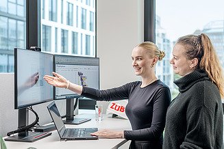 Ein Trainee des Traineeprogramms zeigt auf ihren Bildschirm und stellt eine Frage zum Direkteinstieg bei der Zentralen Technik.