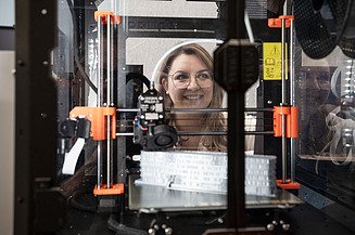 The photo shows a 3D printer and a woman observing the 3D printing process. This is also part of the Zentrale Technik department's engineering expertise