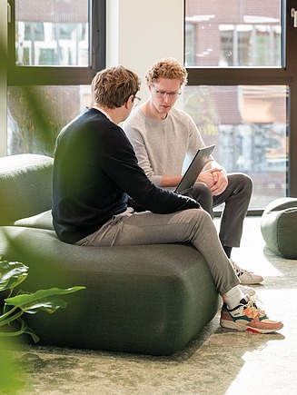 The photo shows two employees from Zentrale Technik sitting on a green sofa and looking at a laptop.