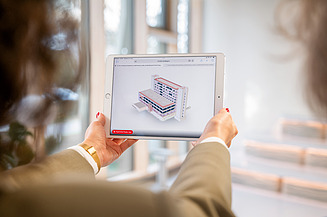 The picture shows a woman holding a tablet on which a BIM model is displayed - a perfect example of smart engineering in digital design.