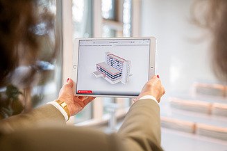 The picture shows a woman holding a tablet on which a BIM model is displayed - a perfect example of smart engineering in digital planning