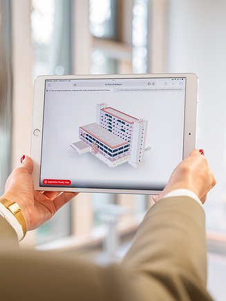 The picture shows a woman holding a tablet on which a BIM model is displayed - a perfect example of smart engineering in digital design.
