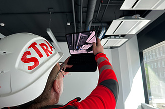 A STRABAG employee documents the installation of MEP systems on the ceiling.