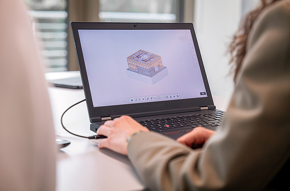 Person arbeitet an einem Laptop mit einem 3D-Gebäudemodell in BIM-Software - Building Information Modeling