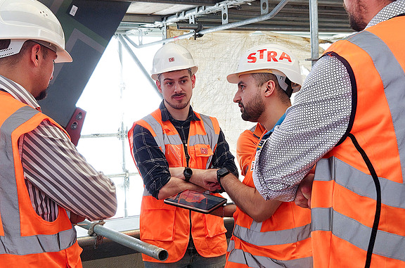 Mehrere Bauarbeiter von STRABAG und der Deutschen Bahn überprüfen Mängel mithilfe von BIM-Modellen auf einem Tablet.