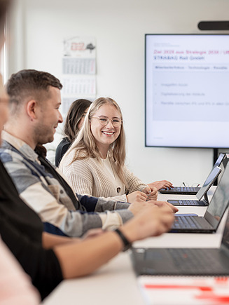Eine Auszubildende lächelt in die Kamera, während sie in einer Besprechung sitzt.
