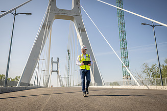 Ein Bauingenieur der Zentralen Technik läuft mit einem Tablet in der Hand über die Satu-Mare-Brücke und begutachtet diese.