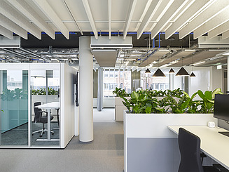 The new open-space office: desks in an open and occasionally closed environment. Sound-absorbing elements hang from the ceiling and office plants improve the indoor climate.