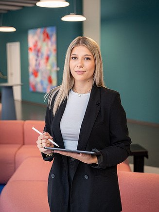A technical systems designer in training stands with a tablet in the Zentrale Technik lounge.