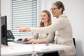 Im Rahmen eines Praktikums oder einer Studierendentätigkeit erhält eine junge Mitarbeiterin an ihrem Schreibtisch eine Erklärung von ihrer Vorgesetzten.