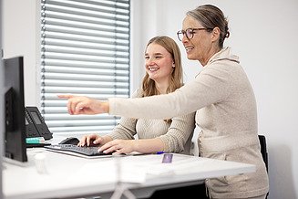 Im Rahmen eines Praktikums oder einer Studierendentätigkeit erhält eine junge Mitarbeiterin an ihrem Schreibtisch eine Erklärung von ihrer Vorgesetzten.