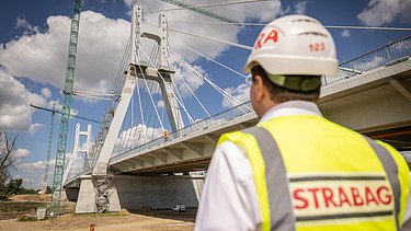 Ein STRABAG-Bauingenieur steht neben einem Zufahrtsviadukt der Satu-Mare-Brücke und blickt auf diese.