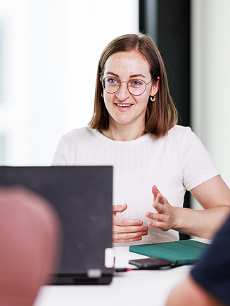 A young employee explains her perspective at the meeting table with colleagues.