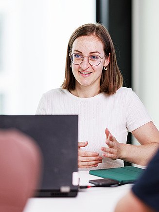 A young employee explains her perspective at the meeting table with colleagues.