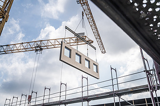 Das Bild zeigt ein Holzmodul, das von einem Kran an seine vorgesehen Stelle gehoben wird.