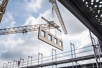 The picture shows a wooden module being lifted into position by a crane.