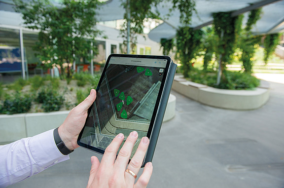 Das Bild zeigt ein Tablet mit einem Kartenausschnitt darauf, der auch im Hintergrund in echt zu sehen ist und symbolisiert damit die Digitalisierung von Standortkarten - GIS in der Zentralen Technik.