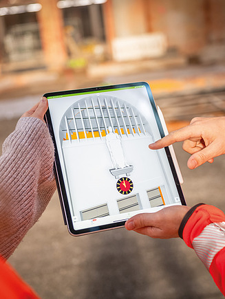 The picture shows two employees from Zentrale Technik standing in an existing building with a tablet. This symbolizes the coming together of design services on the one hand and construction on the other and the joint collaboration.