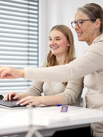 An intern receives an explanation from her supervisor at her desk.