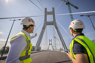 Zwei Bauingenieure der Zentralen Technik blicken auf einen Brückenpylon der Satu-Mare-Brücke.