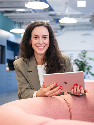 Eine junge Mitarbeiterin hält sitzt in der Lounge der Zentralen Technik und hält ein iPad mit digitalen Baumodellen in der Hand.
