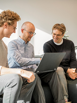 Das Bild zeigt drei Mitarbeiter, die sich über ein nachhaltiges Bauprojekt austauschen.