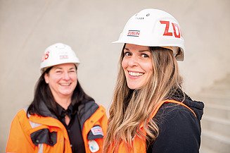 Two experienced engineers stand on the Stuttgart 21 construction site and smile at the camera.