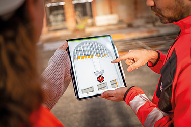 Auf dem Bild sind zwei Mitarbeiter:innen der Zentralen Technik zu sehen, die mit einem Tablet in einem Bestandsgebäude stehen. Dies symbolisiert das Zusammentreffen von Planungsleistung auf der einen Seite und der Bauausführung auf der anderen Seite und die gemeinsame Zusammenarbeit.
