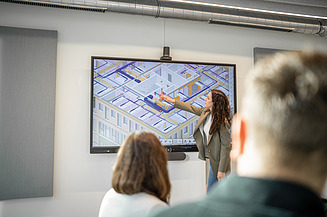 The picture shows an employee of the central technology department pointing at a large screen.