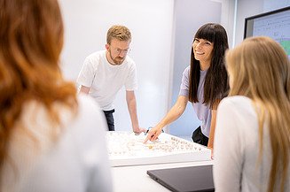 Auf dem Bild sind vier Mitarbeiter:innen der Zentralen Technik zu sehen, die um ein 3D-Modell stehen und sich zu den Ingenieurleistungen nach HOAI austauschen