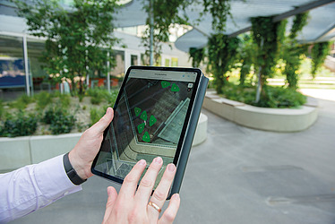 The image shows a tablet with a map section on it, which can also be seen in the background in real life, symbolizing the digitization of location maps