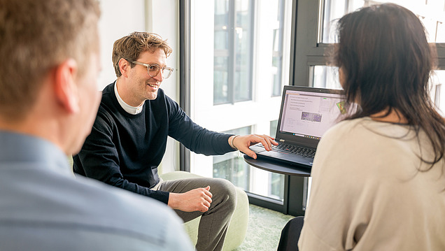Auf dem Bild sind drei Mitarbeitende der Zentralen Technik zu sehen, die vor einem Laptop sitzen und sich über eine Leistungsphase austauschen.