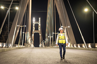 A civil engineer from STRABAG (Zentrale Technik) walks across the brightly lit Satu Mare Bridge at night.