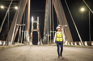 A civil engineer from STRABAG (Zentrale Technik) walks across the brightly lit Satu Mare Bridge at night.