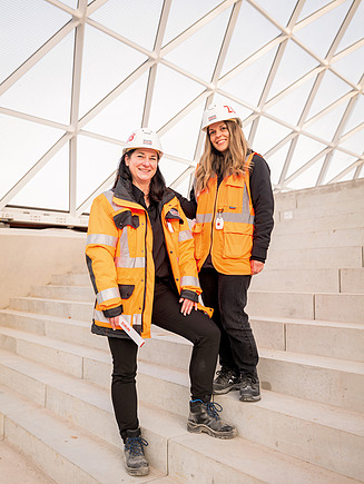 You can see two women in construction site clothing on the building site, who are employed in the engineering office.