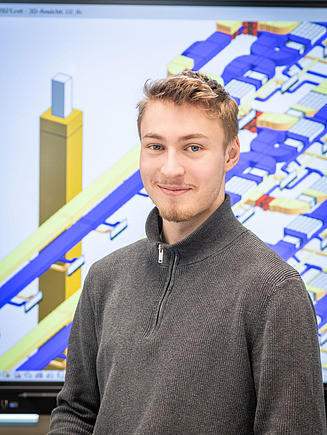 Ein technischer Systemplaner in Ausbildung steht vor einem großen Bildschirm, auf dem ein Plan zu sehen ist.