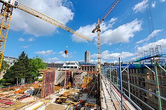 The picture shows several cranes during construction on the roof of the new building with the older HfMT buildings in the background - a perfect symbol for our General Design Contractor services.
