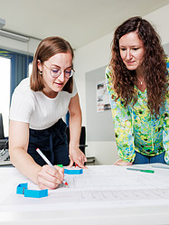 Larina, Auszubildende Bauzeichnerin bei der Zentralen Technik, zeichnet etwas auf einem Bauplan ein.